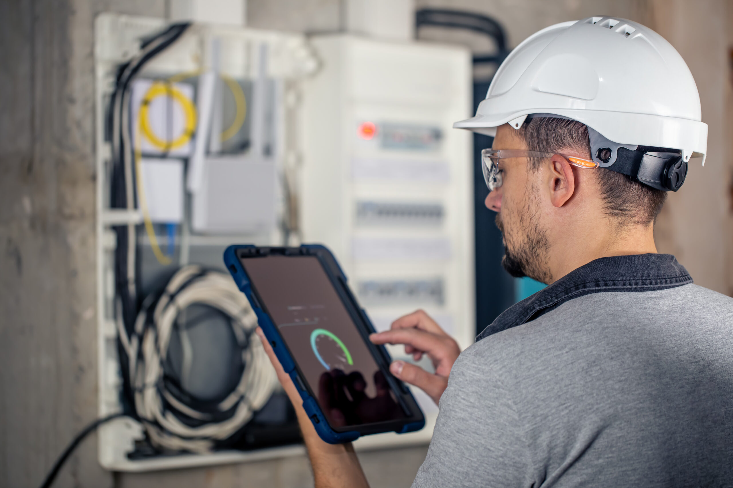 Home man, an electrical technician working in a switchboard with fuses, uses a tablet.